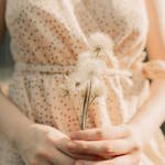 Soft focus image of a woman in a dress gently holding dandelions, capturing a tranquil summer mood.