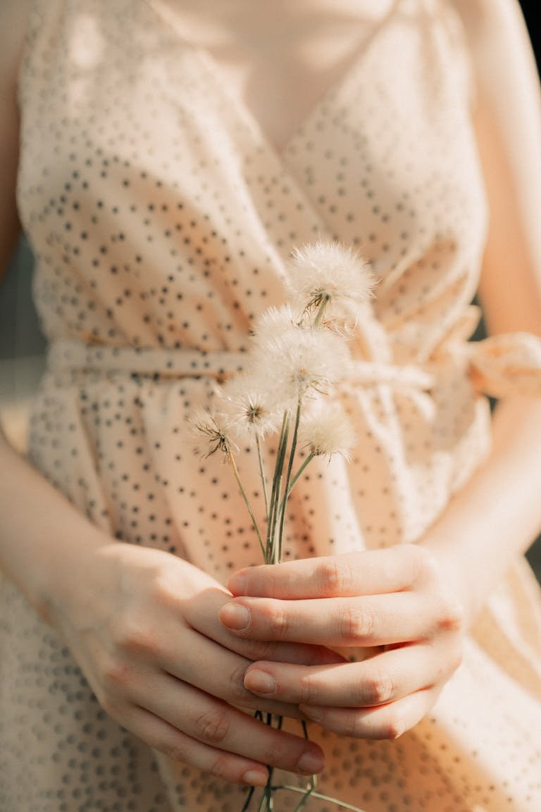 Soft focus image of a woman in a dress gently holding dandelions, capturing a tranquil summer mood.